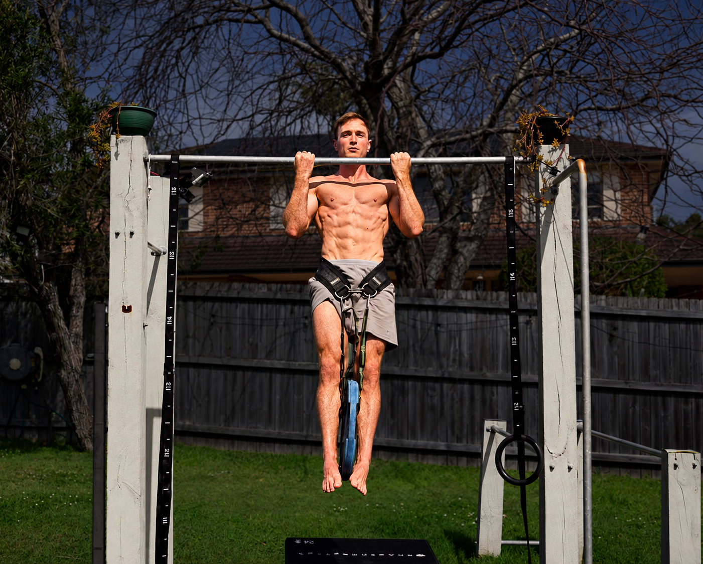 Jake Williams performing a weighted chin-up with his full body and attached weight plates visible